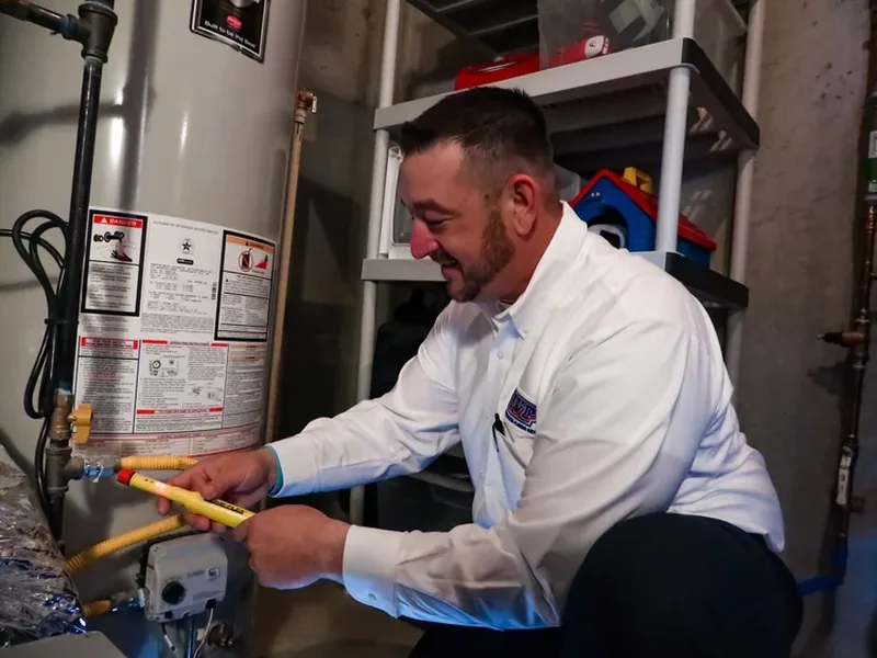 Technician tracing a water heater leak with a flashlight and moisture meter in a Globe garage
